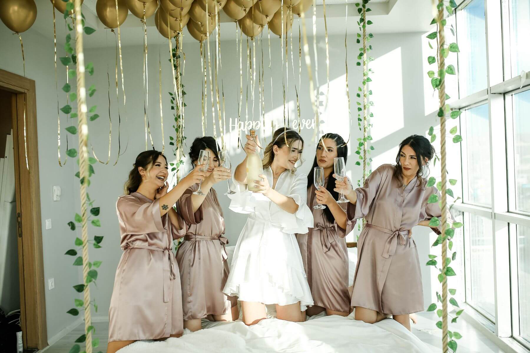 bride and bridesmaids sitting on bed drinking champagne