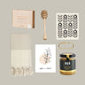 Collection of home and kitchen items including a honey dipper, towel, and honey jar on a neutral background.