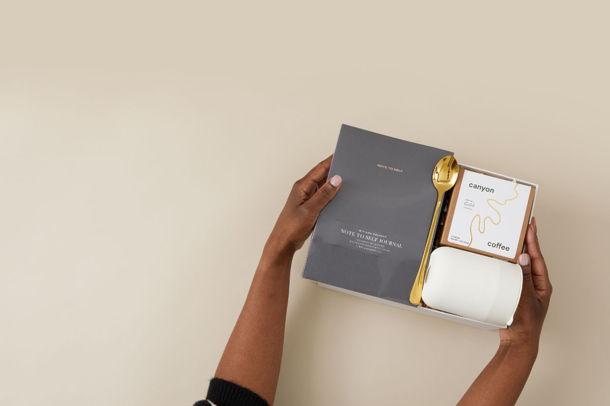 Person holding a coffee gift set with a journal and coffee packaging on a beige background
