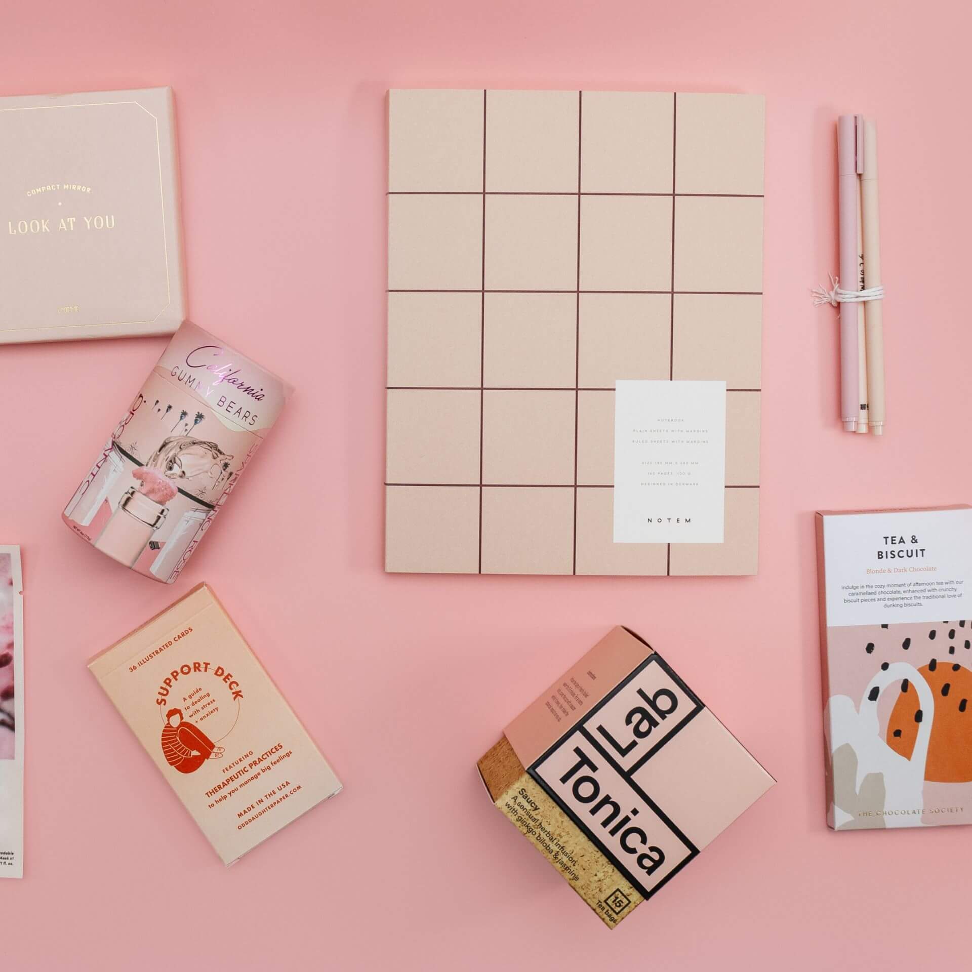 pink gifts - notebook, tea, chocolate, sweets, pens, mirror - against a pink background