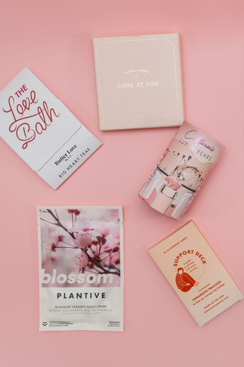 pink gifts - sheet mask, wellness cards, sweets, mirror and bath salts against a pink background
